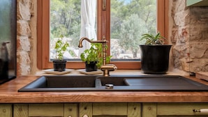 Una cocina con pared de piedra, armarios de madera, un lavamanos y un ventanal con vistas a árboles y una estatua.