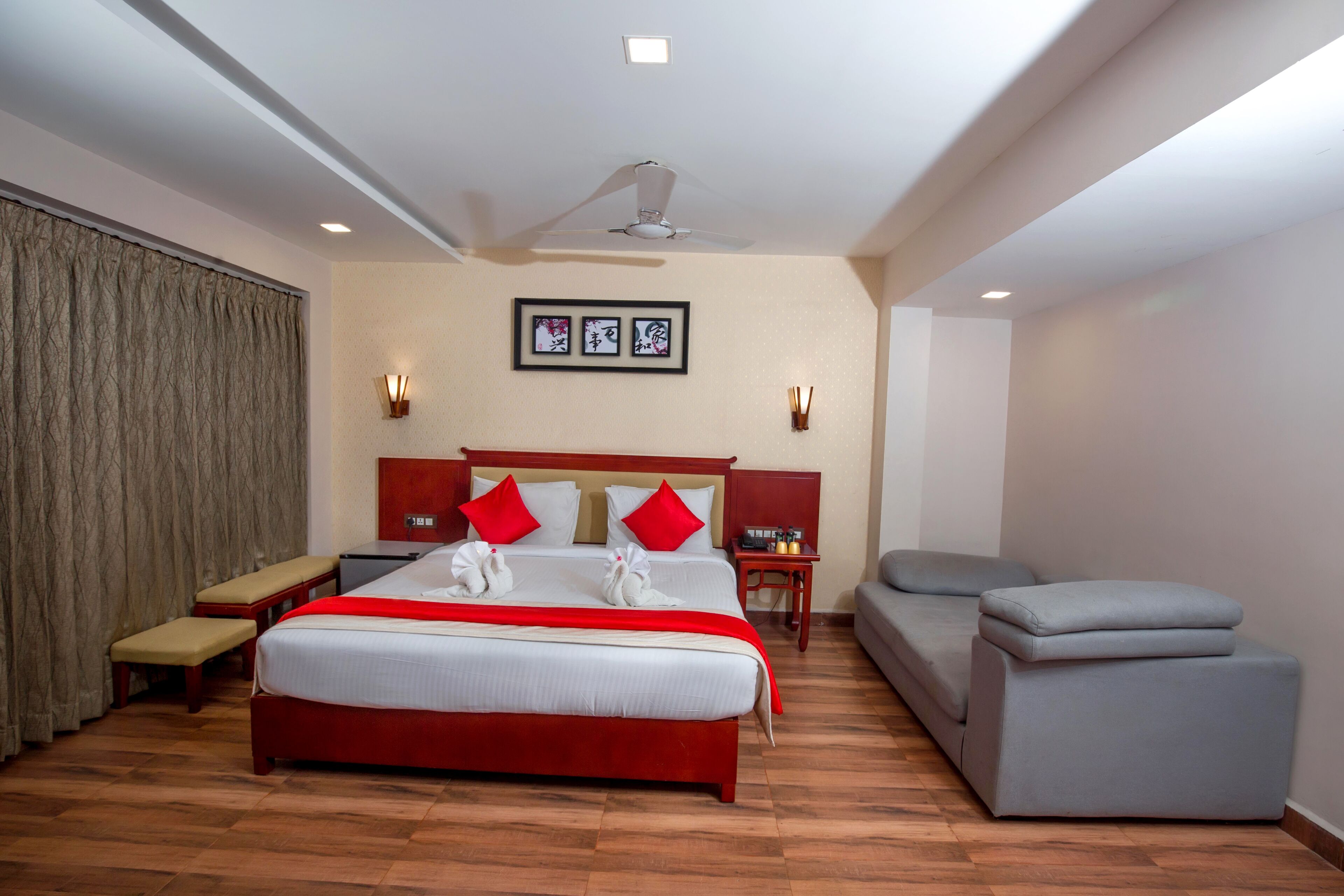 A hotel room with a large bed, a bench, a sofa, a ceiling fan, and a wall-mounted light fixture.