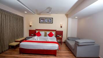 A hotel room with a large bed, a bench, a sofa, a ceiling fan, and a wall-mounted light fixture.
