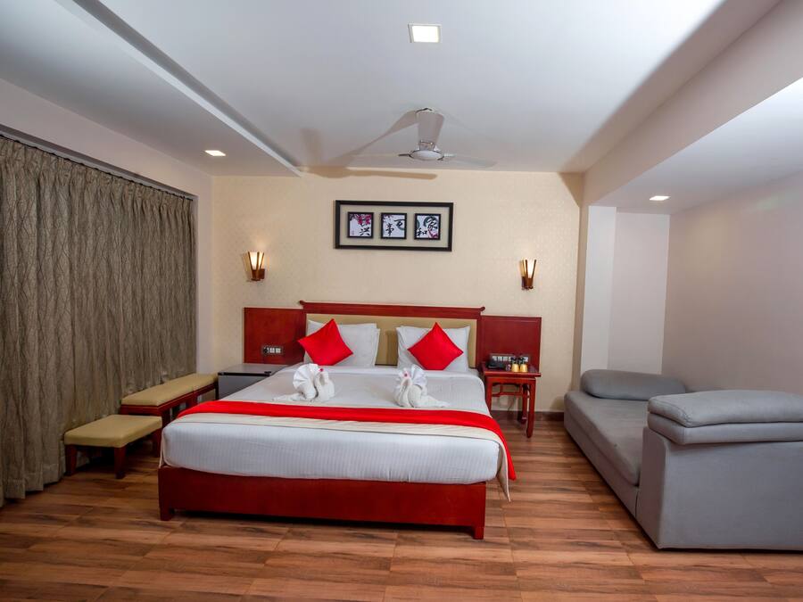 A hotel room with a large bed, a bench, a sofa, a ceiling fan, and a wall-mounted light fixture.