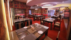 Restaurante com várias mesas e cadeiras, piso de carpete vermelho e arte decorativa nas paredes.
