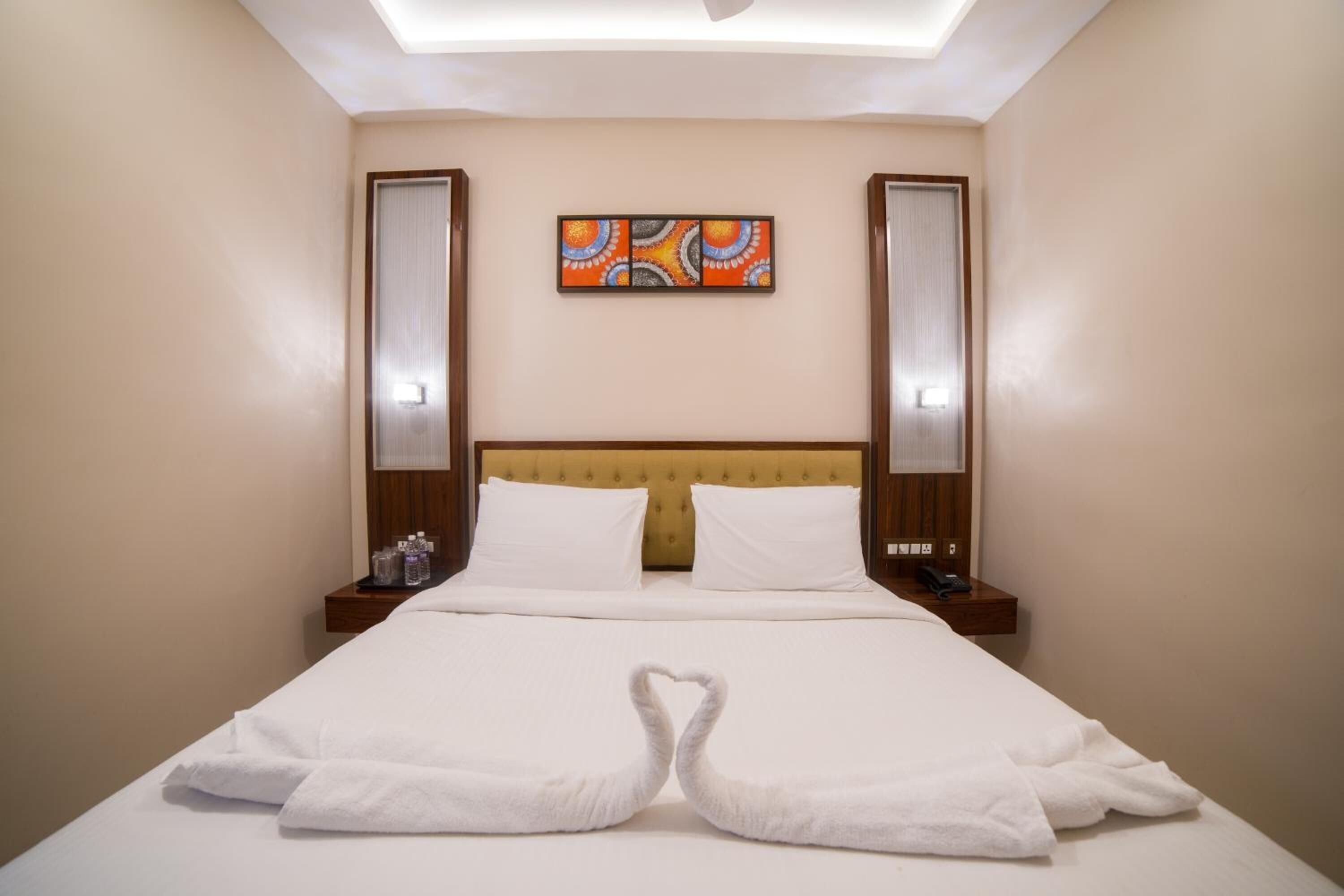 Habitación de hotel con cama, dos mesitas de noche, cabecero y una obra de arte colgada en la pared.