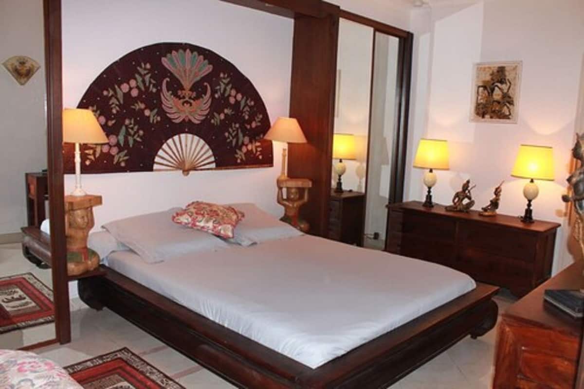 A bedroom with a large bed, two bedside tables with lamps, a mirror, and a decorative wall piece.