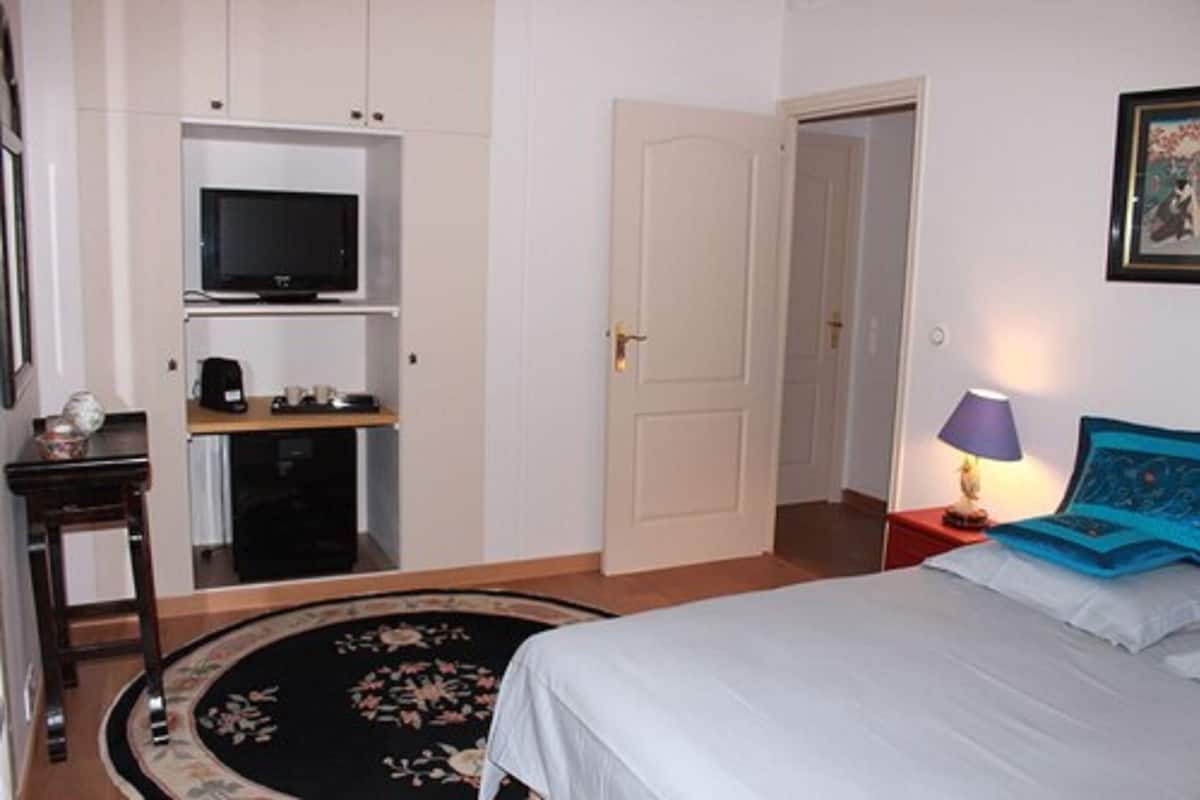 A bedroom with a bed, a TV on a shelf, a door, and a lamp.