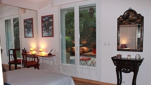 Une chambre à coucher avec un lit, un bureau avec une lampe, une chaise, un miroir et une vue à travers des portes vitrées.