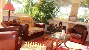 Un salon avec un jeu d’échecs, des meubles en cuir, une lampe et une grande fenêtre donnant sur un paysage verdoyant.