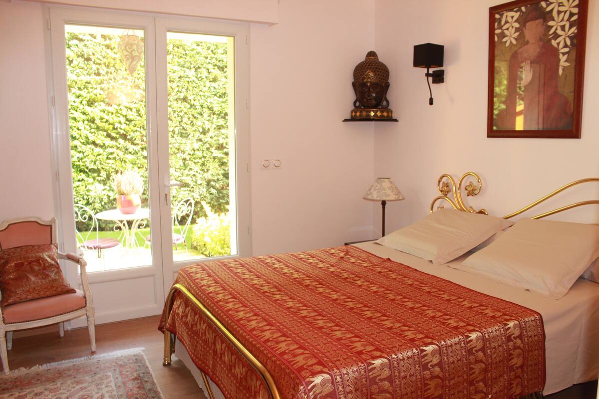 A bedroom with a bed, a chair, a lamp, and a window with a view of greenery.