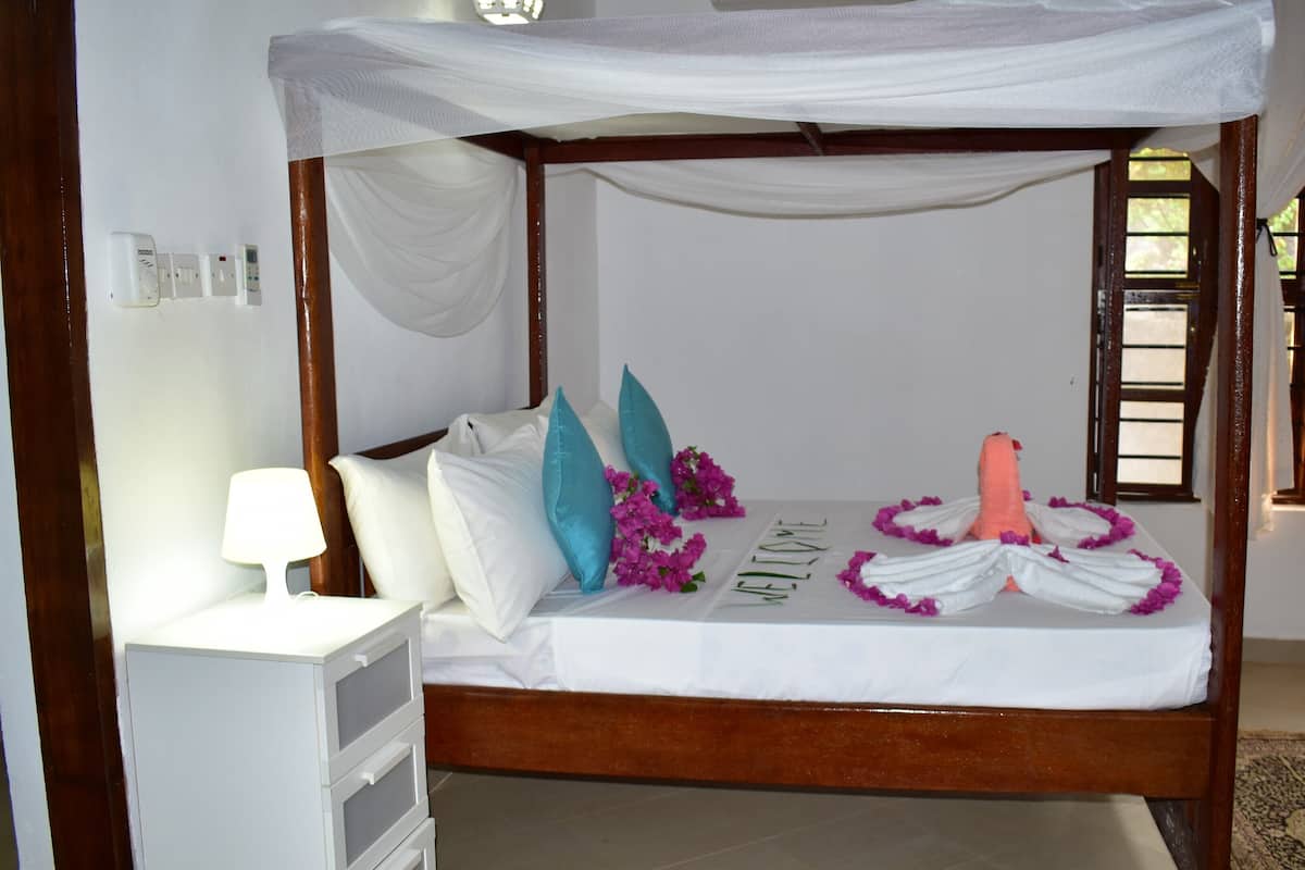 Una cama con dosel, ropa de cama blanca, almohadillas verde mar y flores decorativas.