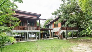 A two-story wooden house with a balcony, a covered porch, and a truck parked in the driveway. - Jule Red Villa, Wifi, AC, Balcony, Terrace (Ko Pha-ngan)