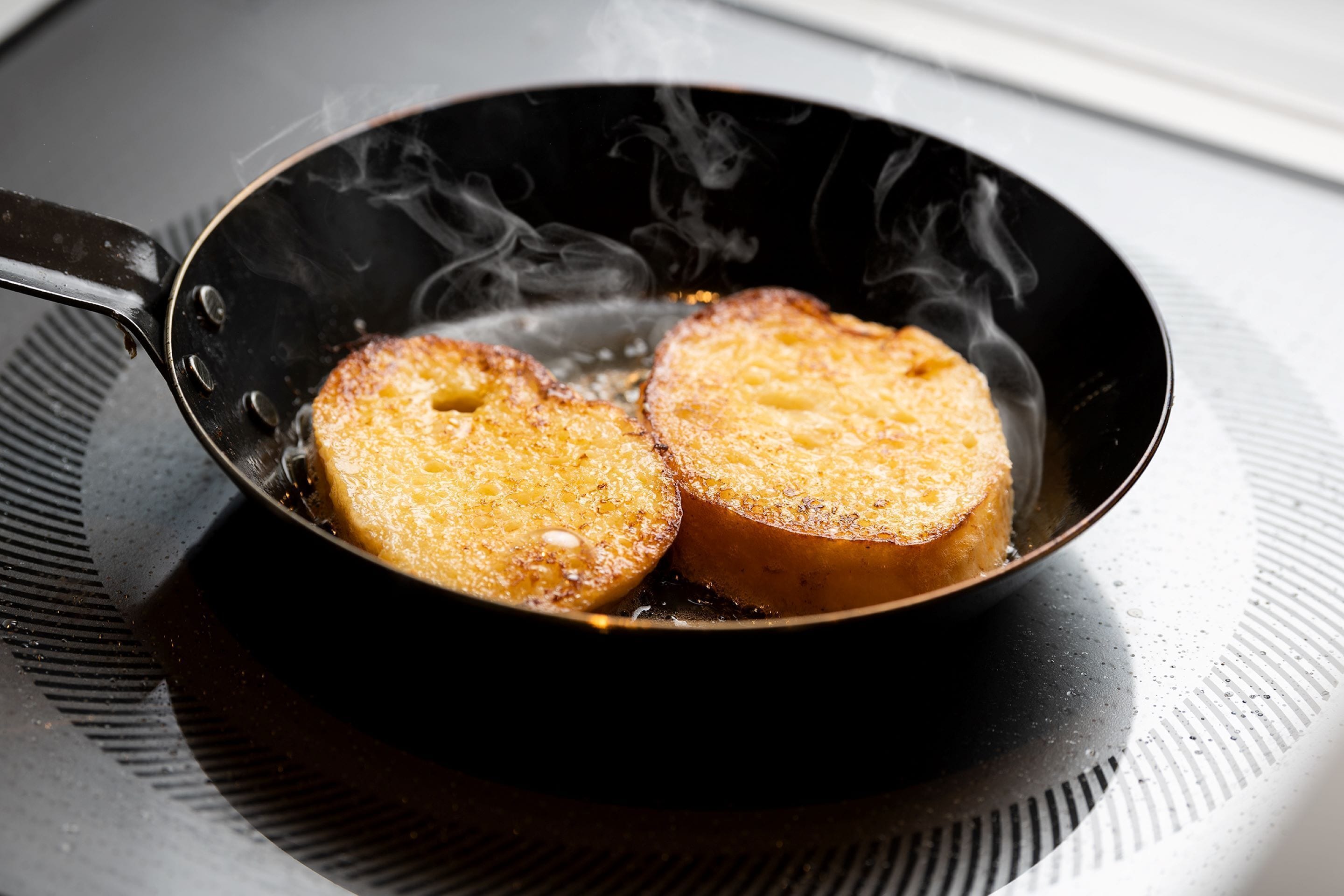 A frying pan with two slices of bread cooking on a stovetop.