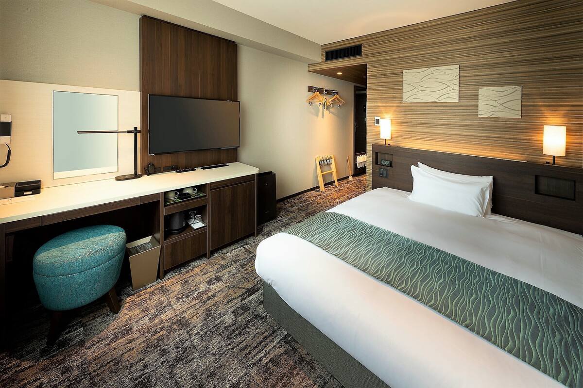 Una habitación de hotel con cama, escritorio, televisor y espejo.