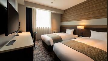 A hotel room with two beds, a desk, a TV, and a window with curtains.