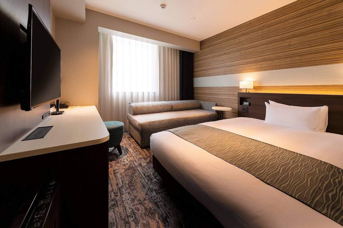 Una habitación de hotel con una cama grande, un sofá, un escritorio y un televisor.