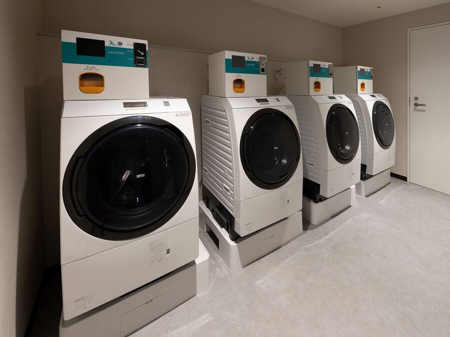 A row of four front-loading washing machines in a laundry room with a private door.