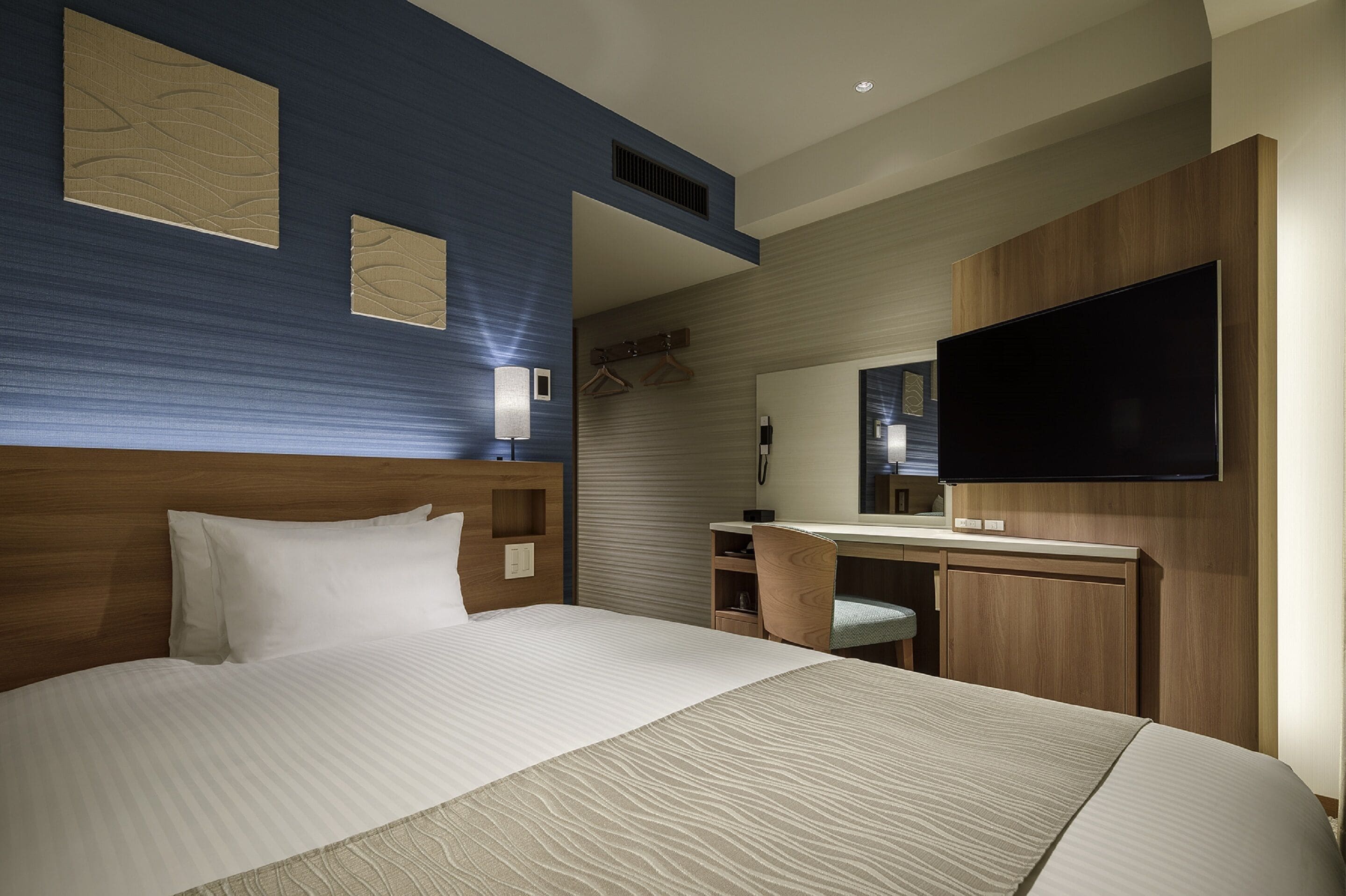 Habitación de hotel con una cama grande, un escritorio con silla, un televisor de pantalla plana y un espejo.