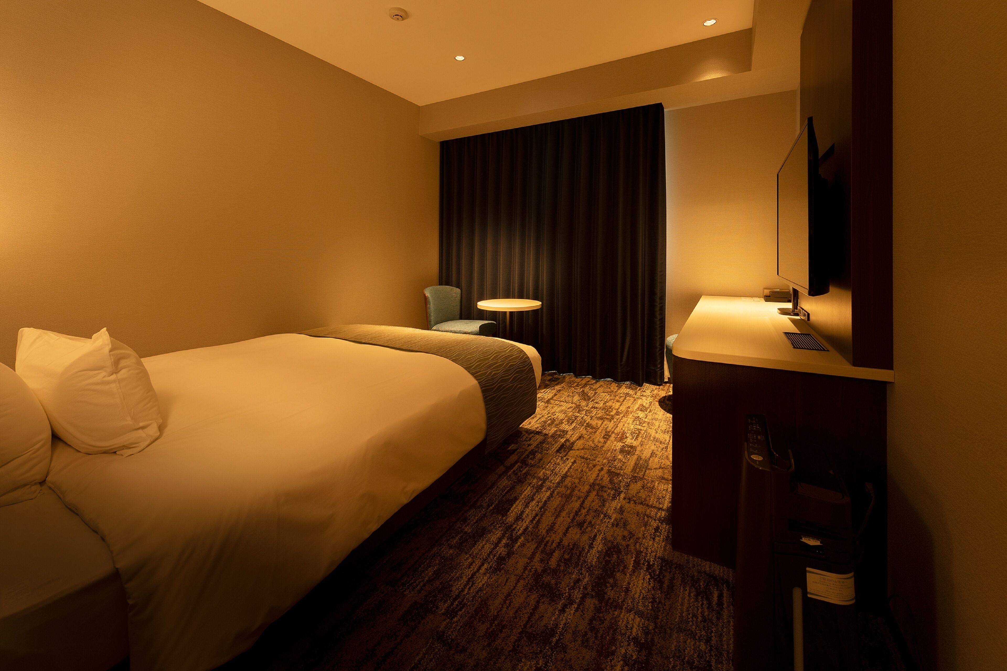 A hotel room with a large bed, a smaller bed, a desk with a mirror, a chair, and a large window with curtains.