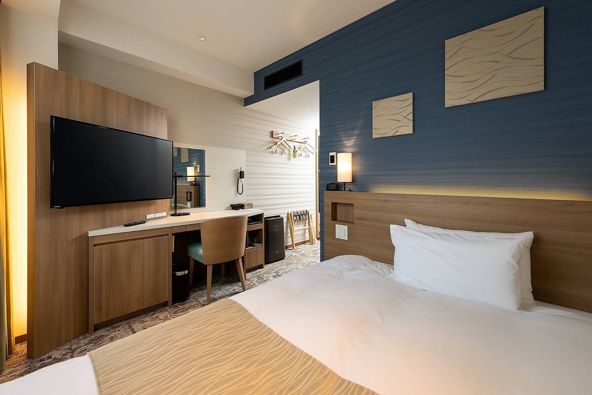 Una habitación de hotel con cama, escritorio, silla, televisor y obras de arte en las paredes.