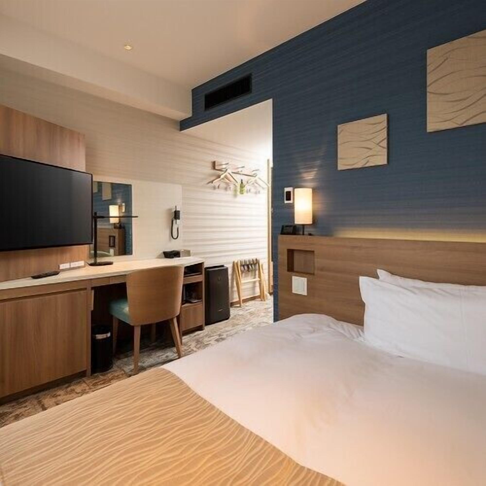 Habitación de hotel con cama, escritorio, silla, televisión y una obra de arte en la pared.