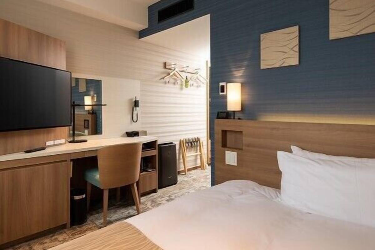 Habitación de hotel con cama, escritorio, silla, televisión y una obra de arte en la pared.