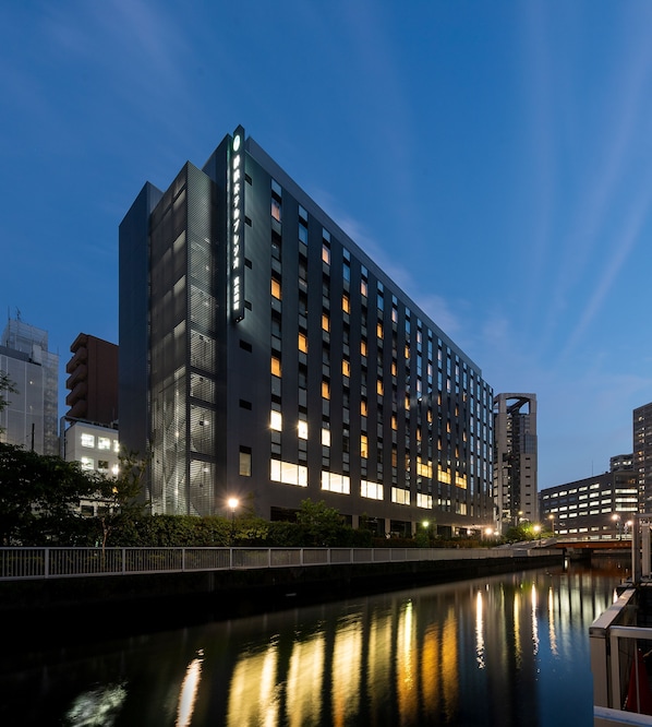 Hotel moderno con un espejo de agua reflectante al frente, destacándose por su diseño vertical y múltiples ventanas iluminadas.