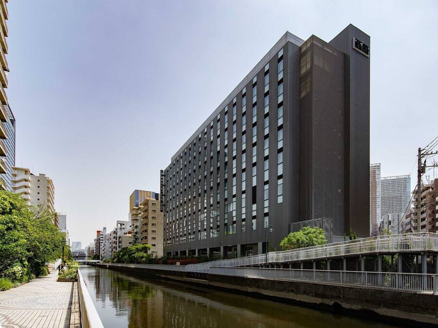 A modern building with a long facade, a waterway in front, and a pedestrian bridge.