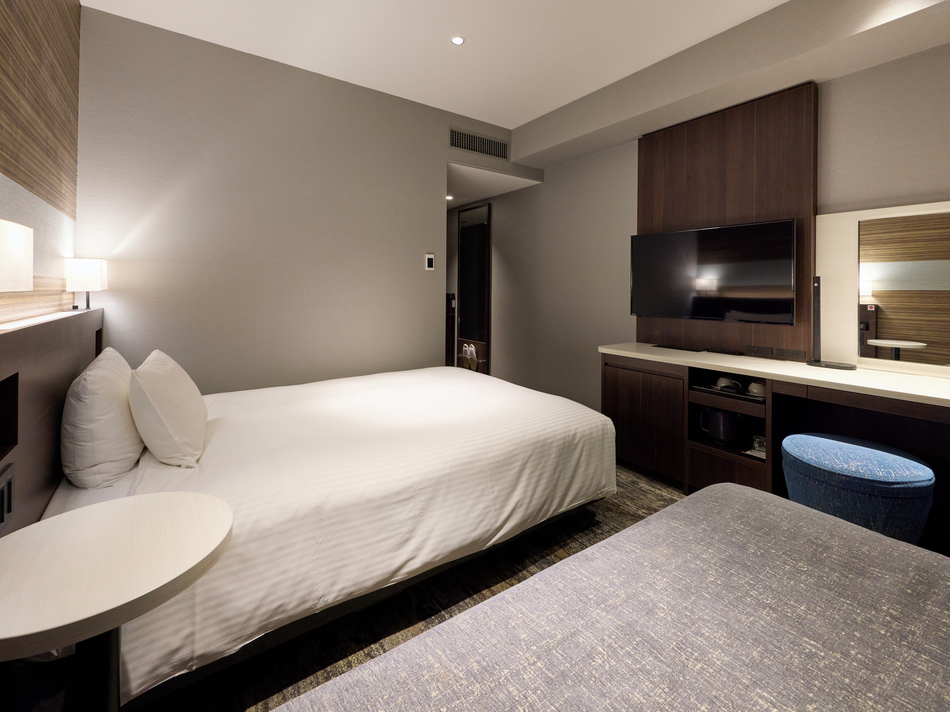 Una habitación de hotel con una cama, un escritorio, un televisor y un taburete pequeño.
