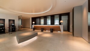 A modern reception area with a curved reception desk, two digital kiosks, and a minimalist design. - Shizutetsu Hotel Prezio Tokyo Tamachi (Tokyo)
