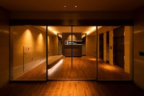 Un hall de hotel con suelo de madera, puertas de cristal y un cartel que indica el camino al hall.