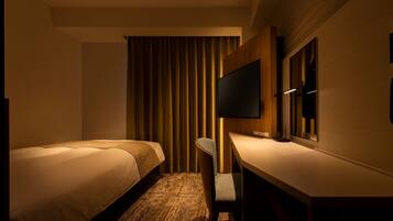 A hotel room with two beds, a desk, a chair, a flat-screen TV mounted on the wall, and a large window with curtains.