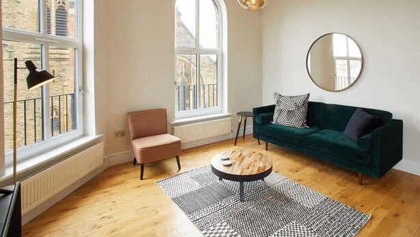 Ein modernes Wohnzimmer mit einem grünen Sofa, einem runden Couchtisch und einem großen Fenster mit Blick auf ein Gebäude.