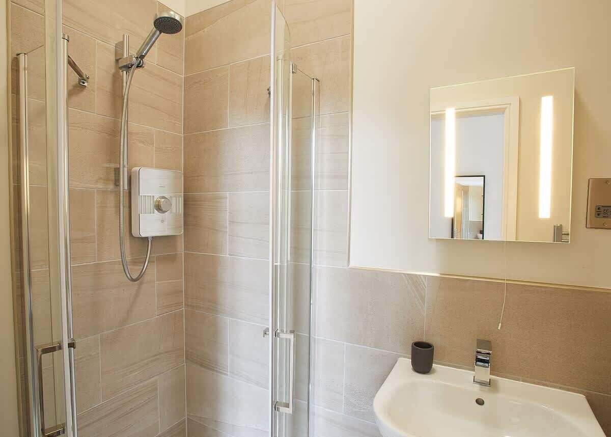 A modern bathroom with a glass-enclosed shower, a white sink, and a mirror with integrated lighting.