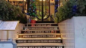 Eine Treppe führt zu einem Café, das mit einem Weihnachtsbaum und beleuchteten Schildern für verschiedene Speisen und Getränke dekoriert ist.