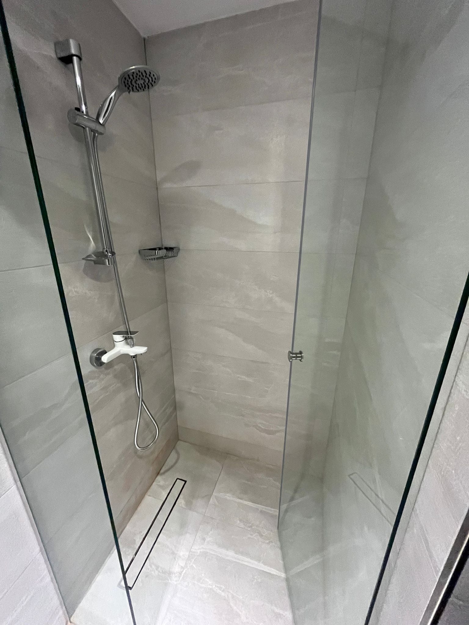 Cabina de ducha con paredes de vidrio, ducha de mano y ducha empotrada en la pared.