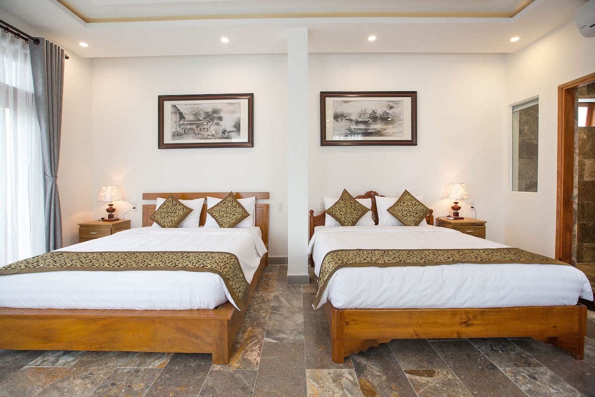 Ein Hotelzimmer mit zwei hölzernen Betten, weißer Bettwäsche und Zierkissen. An den Wänden sind Wandleuchten und gerahmte Kunstwerke über den Betten angebracht.