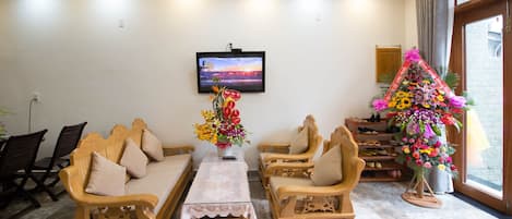 Una sala de estar con sofá, sillas, una mesa de centro, televisor y un arreglo floral.