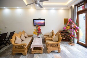Uma sala de estar com sofá, cadeiras, mesa de centro, televisão e um arranjo floral.
