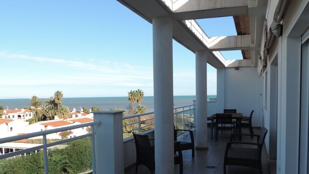 Uma varanda com vista para o mar, com uma mesa e cadeiras.