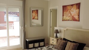 Quarto com uma cama grande, uma mesa de cabeceira, um banco com cestos, um quadro e uma porta de correr para o exterior.