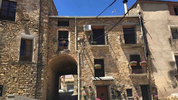 A stone building with an arched passageway, balconies with flower boxes, and a clear blue sky. - Tato House -Figuerola d'Orcau- (Figuerola de Orcau)