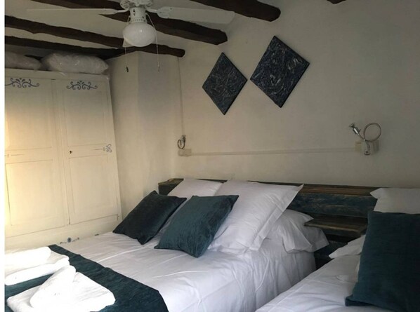 Un dormitorio con techo de madera, cama con ropa de cama blanca y aguamarina, y dos lámparas fijadas a la pared.
