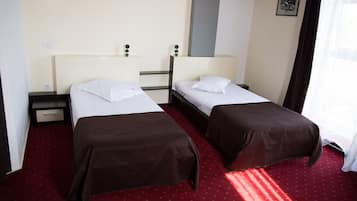 A hotel room with two single beds, a small table, and a nightstand.