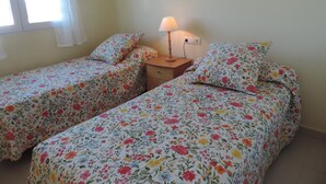 A bedroom with two single beds, a bedside table with a lamp, a picture on the wall, and a window with curtains.