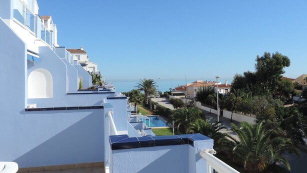 A balcony with a clear view of a swimming pool and palm trees, overlooking a coastal area with buildings.