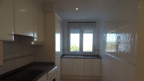 A compact kitchen with a washing machine, a sink, and a window with blinds.
