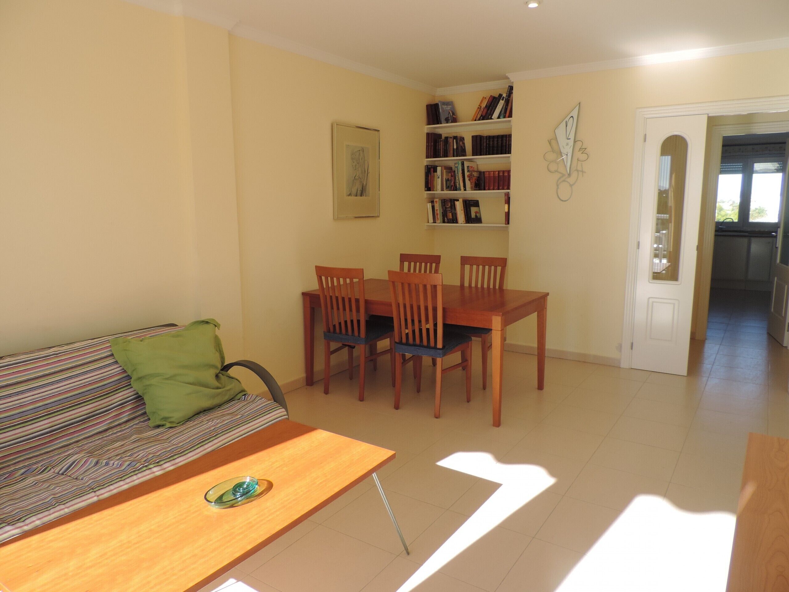 Una sala de estar con un sofá, una mesa de madera y un comedor con sillas y una estantería.