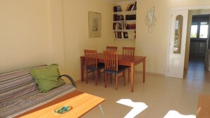 A living room with a sofa, a wooden table, and a dining area with chairs and a bookshelf.