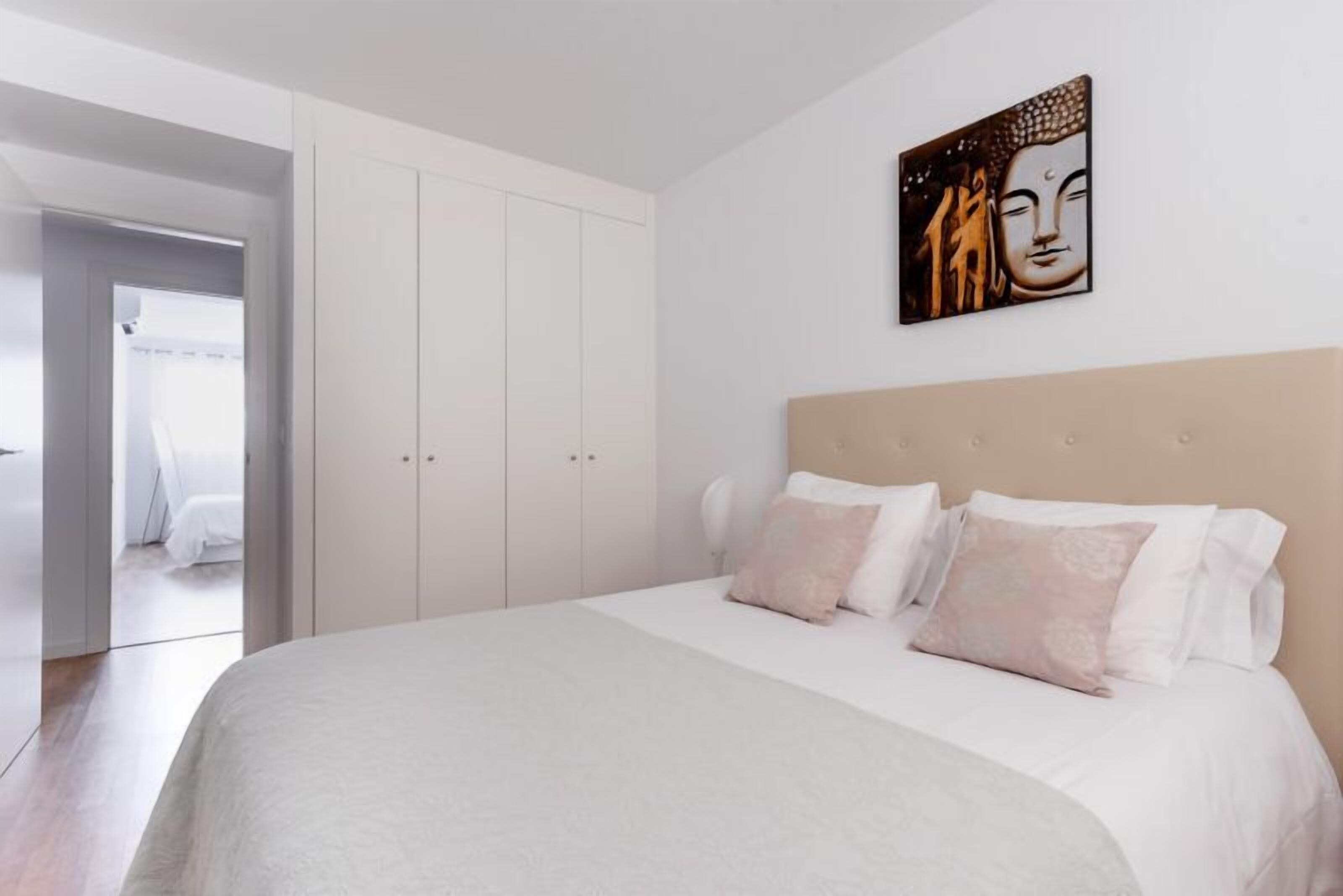 Un dormitorio con una cama grande, paredes blancas, un cabecero de madera y un cuadro de Buda.