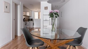 A modern dining area with a glass table and two chairs, a vase with flowers, and a kitchen in the background. - Salamandra Altea 17 By Vero (Altea)