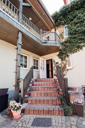 A building with a wooden balcony, brick steps, and potted plants. - Hotel Garni Rank (Bad Berka)