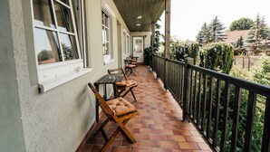 A covered balcony with tiled flooring, wooden furniture, and a view of the surrounding greenery. - Hotel Garni Rank (Bad Berka)